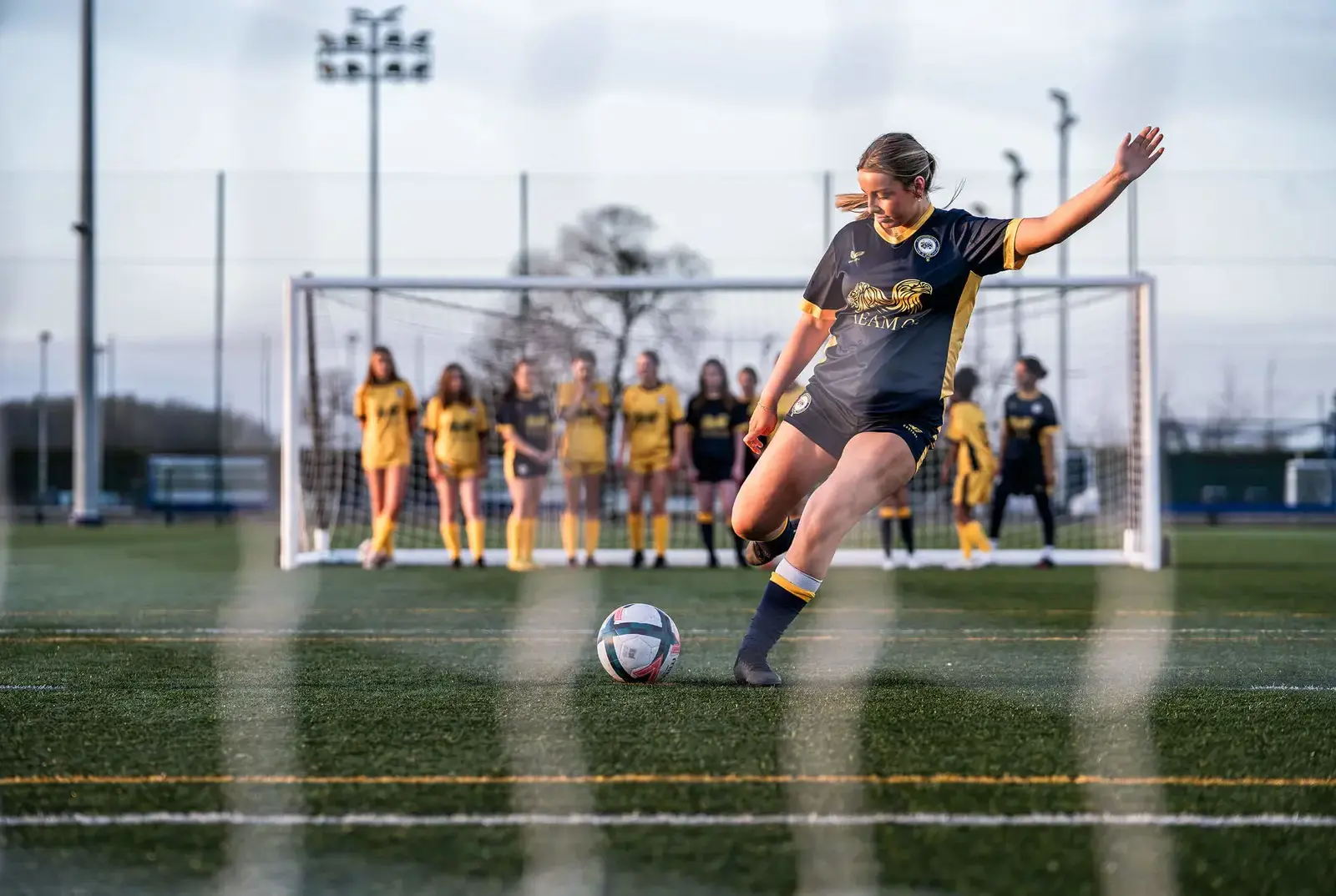 Girl scoring a goal during a penalty shoot-out on Queen Ethelburga's football pitch.